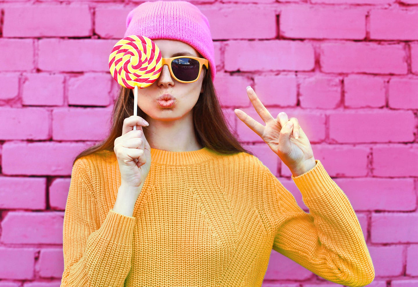 Woman with glasses. Holding a lolipop and signing a peace sign