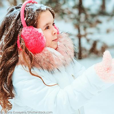 Young girl playing in the snow wearing trendy accessories like a pink headband with pom poms to cover her ears and matching glvoes